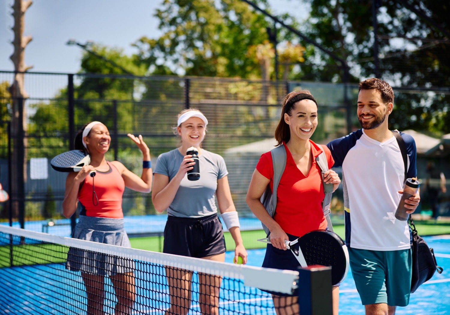 Four players walking off a bright blue court together, smiling