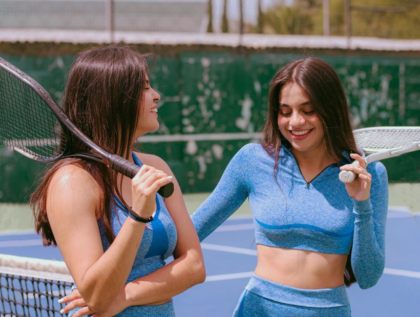 Two women in blue activewear with rackets on a tennis court